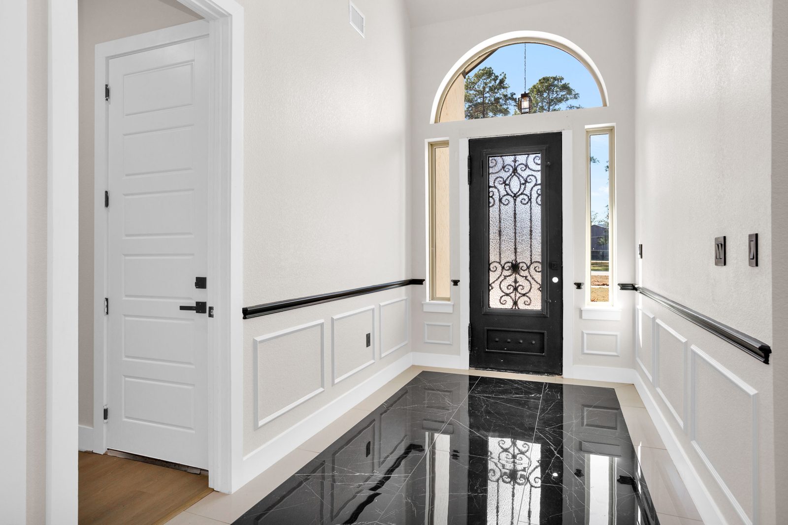Foyer with black marble floor, wainscoting and iron door